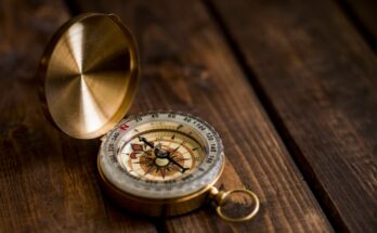 A vintage brass compass displayed on a wooden surface, with its lid open, indicating direction.