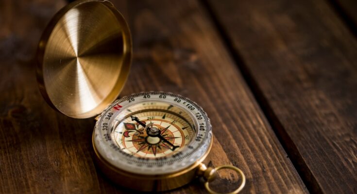 A vintage brass compass displayed on a wooden surface, with its lid open, indicating direction.